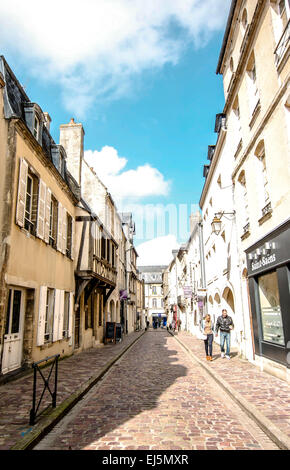 La gente cammina in una piccola strada di ciottoli nel quartiere dello shopping di Bayeux in Normandia, Francia su una luminosa e soleggiata giornata. Foto Stock