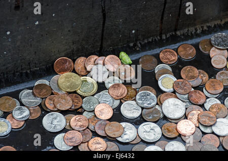 I turisti in attesa per il ferry diretto alla Statua della Libertà gettare monete provenienti da molti paesi nel canale di scolo del dock, New York. Foto Stock