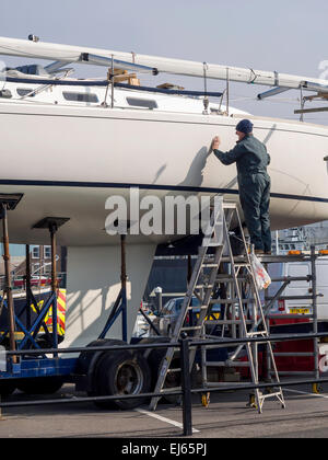 L'uomo la pulitura e la verniciatura di una barca a vela a Whitby North Yorkshire Regno Unito Foto Stock