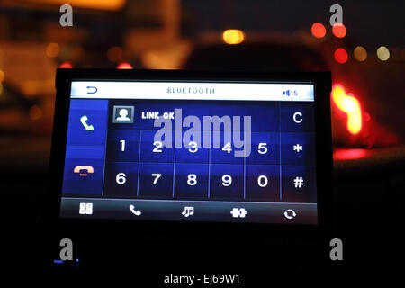 Telefono cellulare bluetooth nella schermata di collegamento nel cruscotto del veicolo nel traffico di notte Foto Stock