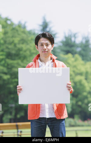 I giovani giapponesi sorridente uomo con pannello bianco in un parco Foto Stock