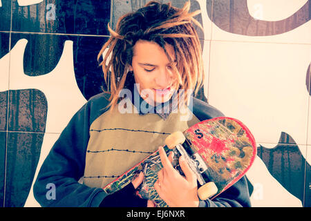 Ritratto di giovane ragazzo con skate e capelli rasta in un concetto di stile di vita caldo filtro applicato Foto Stock