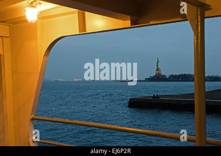 Il Porto di New York visto al crepuscolo da un traghetto, con le luci delle navi sotto la Statua della Libertà. Foto Stock