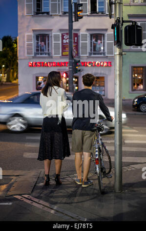 Coppia Giovane aspettando in attraversamento pedonale, spostamento auto, notte Strasburgo Alsace Francia Europa Foto Stock