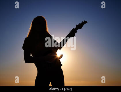 Silhouette di donna busker davanti a sunrise. Corpo di piegatura del musicista femmina mantenendo la chitarra al sorgere del sole sullo sfondo Foto Stock