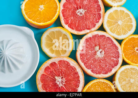 Succose arance, limoni e pompelmi con uno spremitore su sfondo blu Foto Stock