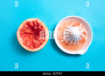 Juiced pompelmo rosso con uno spremitore su sfondo blu Foto Stock