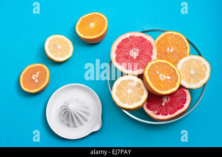 Le arance e i limoni pompelmi rosa in una ciotola e uno spremitore su uno sfondo blu Foto Stock