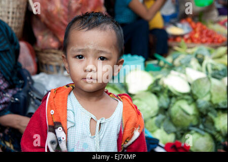Un piccolo ragazzo in piedi di fronte a verdure fresche in un Rangoon mercato alimentare di Myanmar (Birmania) Foto Stock