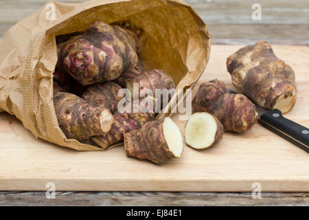 Carciofi di Gerusalemme in un sacchetto di carta su un tagliere di legno con un piccolo coltello di abbinamento Foto Stock