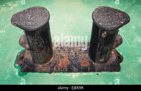 Vecchio arrugginito nero bollard montato su verde ponte di nave Foto Stock