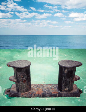 Vecchio arrugginito nero bollard montato sulla nave verde deck, con panorama sul mare su uno sfondo Foto Stock