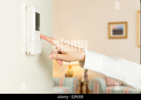 Signora caucasica premendo il termostato moderno Foto Stock