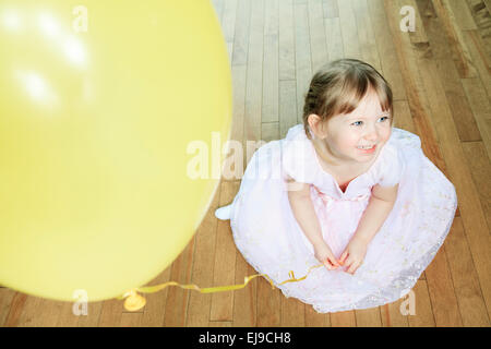 Una bella bambina Siediti sul pavimento con un palloncino Foto Stock