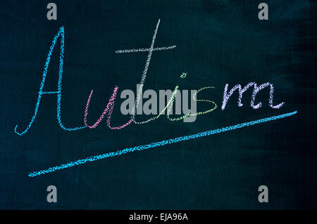 La parola autismo con le sue lettere scritte con il gesso di diversi colori su una lavagna verde Foto Stock