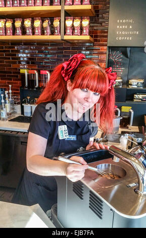 Dai capelli di fiamma barista presso una caffetteria Starbucks fruste su una delle loro estremità alta caffè gourmet realizzato con la costosa macchina di trifoglio Foto Stock