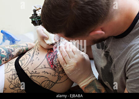 Close-up di tattooist disegna sulla ragazza hip Foto Stock