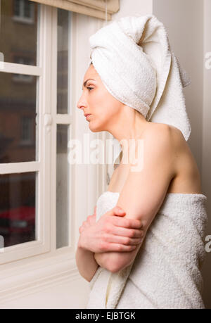 Giovane donna che guarda fuori da una finestra dopo una doccia. Foto Stock