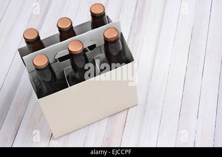 Alta angolazione di un fustellato da sei confezioni di birra bruna bottiglie su un rustico di legno bianco tavola. Formato orizzontale con copia spazio. Foto Stock