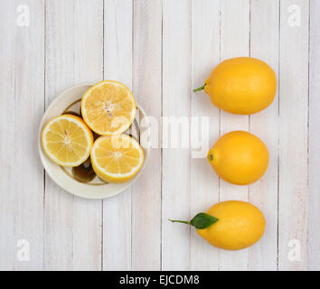 Angolo alto ancora la vita di tre limoni interi e tre metà di limone in una ciotola su un rustico di legno bianco tavolo da cucina. Foto Stock