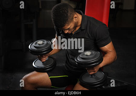 Giovane uomo seduto su un banco di lavoro in palestra Foto Stock