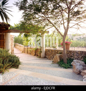 Lastricate di ciottoli passi e il percorso che conduce alla pergola in pietra nel grande giardino in Maiorca Foto Stock