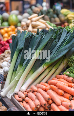 Fresche porri e carote visualizzata su un vegetale in stallo contro uno sfondo di un assortimento di frutta e verdura Foto Stock