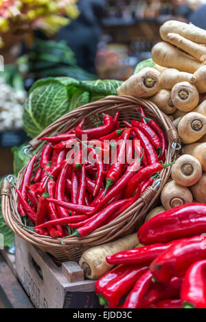 Un cesto di peperoncini rossi visualizzata su uno stallo vegetali contro uno sfondo di pastinaca e cavolo Foto Stock