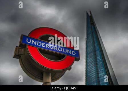 Una stazione della metropolitana di Londra segno mostrato con la Shard de-focalizzato in background Foto Stock