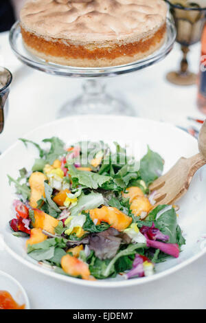 Una fresca insalata di foglie giovani, fette di pesche e di una torta con topping di meringa. Foto Stock