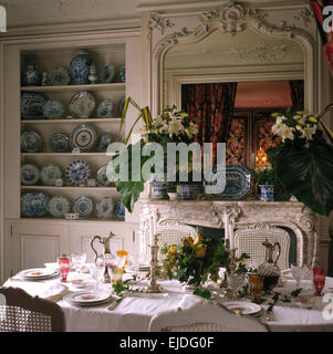 Gigli bianchi e le grandi foglie in vasi su mantelpiece sotto lo specchio ornati degli anni novanta in sala da pranzo con alcova armadio Foto Stock