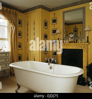 Sala stampa carta da parati in bagno di colore giallo con roll top bagno davanti al caminetto Foto Stock