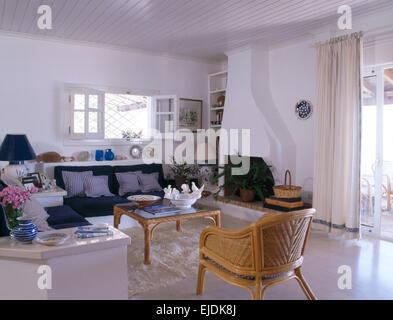 La canna da zucchero sedia e tavolo da caffè in costiera stanza vivente con cuscini blu sul divano montato Foto Stock