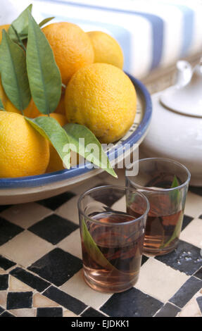 Limoni freschi in una ciotola blu su un tavolo piastrellato con bicchieri di tè alla menta Foto Stock