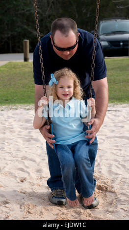 Papà oscillando la sua quattro anni alla figlia di un parco giochi per bambini Foto Stock