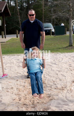 Papà oscillando la sua quattro anni alla figlia di un parco giochi per bambini Foto Stock