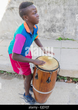 Vista laterale di un 10-12 anni ragazzo afro-cubane giocando conga tamburo nelle strade di Regla, Cuba al di fuori della sua casa.. Foto Stock