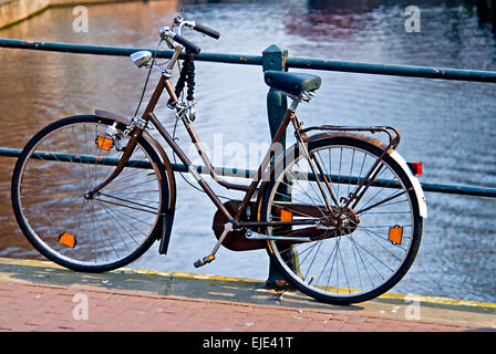 Bicicletta appoggiata contro le ringhiere su un ponte sul canale di Amsterdam Foto Stock