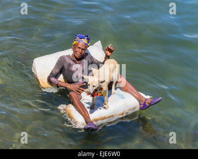 Una femmina di afro-cubane mendicante sdraiato su una zattera nell'oceano di Cayo Granma. Ella è accompagnato dal suo cane bianco. Foto Stock