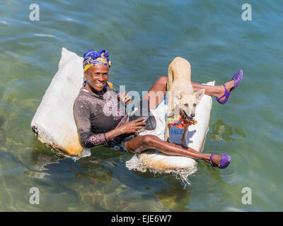 Una femmina di afro-cubane mendicante sdraiato su una zattera nell'oceano di Cayo Granma. Ella è accompagnato dal suo cane bianco. Foto Stock