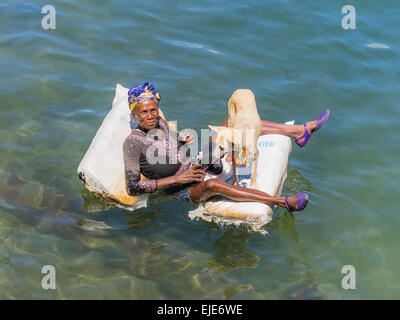 Una femmina di afro-cubane mendicante sdraiato su una zattera nell'oceano di Cayo Granma. Ella è accompagnato dal suo cane bianco. Foto Stock