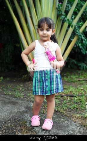 Ragazza 4 anni, tenendo una bambola Barbie, che pongono di fronte a un albero di palma, San Juan de Nicaragua o San Juan del Norte o Graytown Foto Stock