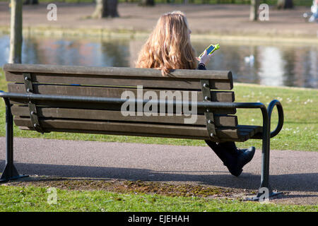 Giovani donne controllo telefono cellulare sat su banco sul terrapieno in Bedford, Bedfordshire, Inghilterra Foto Stock