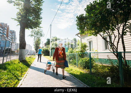 GOMEL, Bielorussia - Giugno 10, 2014: Unidentified donna anziana con una benna carrello rotola giù la strada, di Gomel in Bielorussia Foto Stock