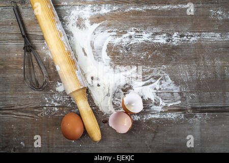 Uova, gusci d'uovo, la farina e il perno di rotolamento su sfondo di legno. Vista dall'alto. Foto Stock