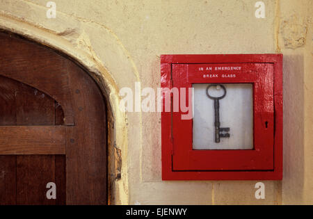 Antica porta di legno a parete spessa con casella rossa contenente grande chiave di antiquariato e istruzioni in caso di emergenza rompere il vetro Foto Stock