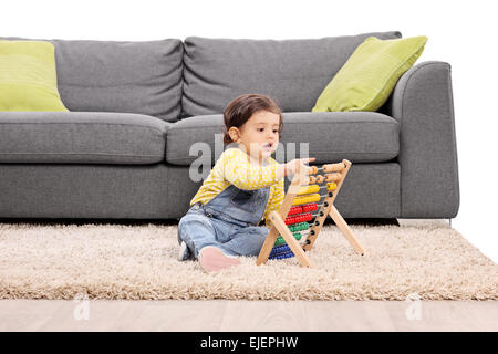 Bambina gioca con un abaco seduto sul pavimento da un moderno edificio grigio divano isolati su sfondo bianco Foto Stock