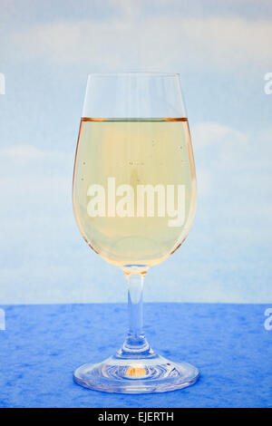 Bicchiere di vino bianco su un tavolo blu con un cielo blu sullo sfondo Foto Stock