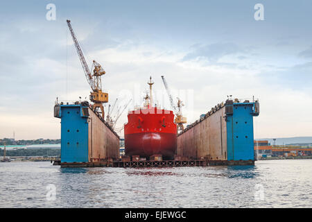 Floating blu dock a secco con la petroliera rossa sotto la riparazione all'interno, vista frontale Foto Stock