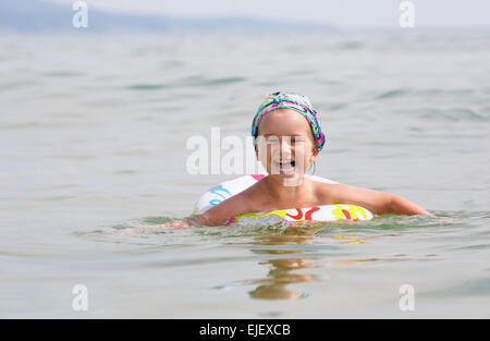 Bambino felice nuota nel mare su anello gonfiabile in una limpida giornata di sole. Profondità di campo. Focus sul modello. Foto Stock